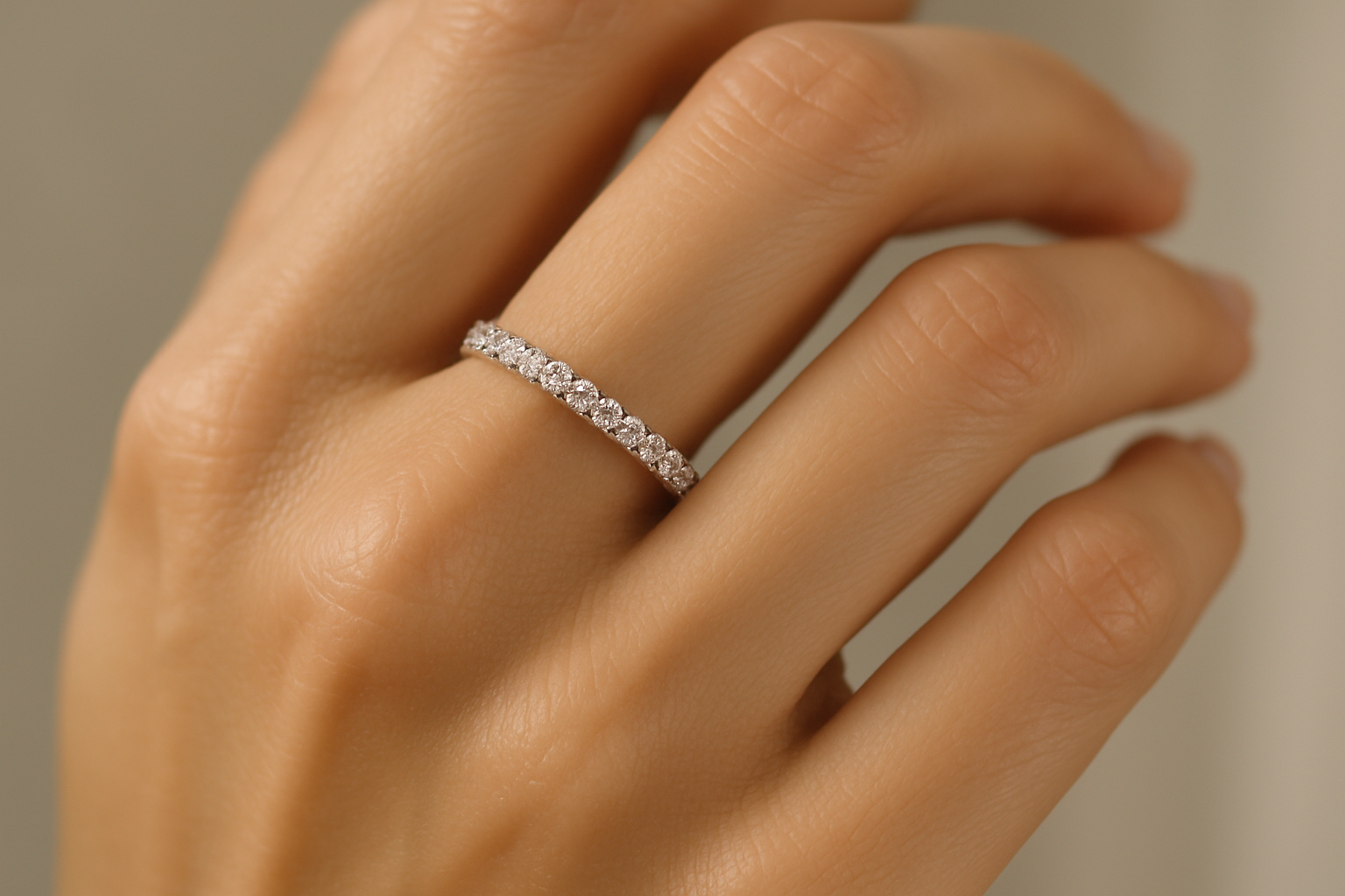 Close-up photograph of a woman's well-manicured hand wearing a sparkling diamond eternity band in white gold or platinum